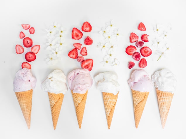 six waffle cones with pink and white ice cream decorated with strawberries and flowers