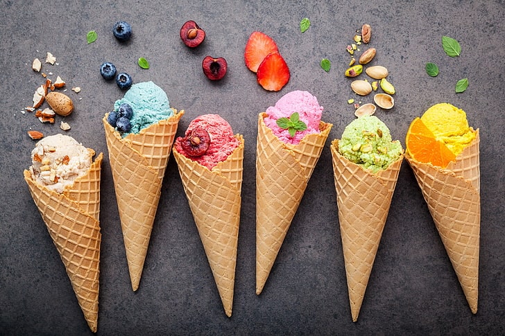 six waffle cones with different types of colorful ice cream decorated with nuts, berries and leaves